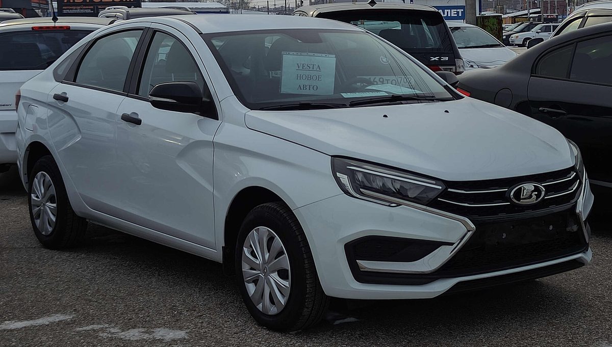 Белая Lada Vesta на территории автосалона в России, на лобовом стекле табличка «Vesta новое авто»