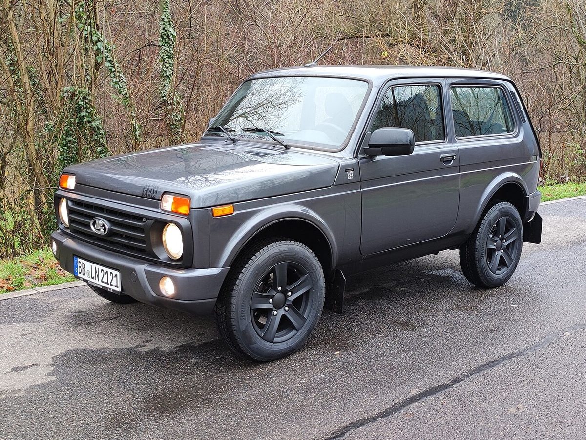 Серая трёхдверная Lada Niva Legend в исполнении Urban 2021 года выпуска на мокрой дороге, вид спереди сбоку